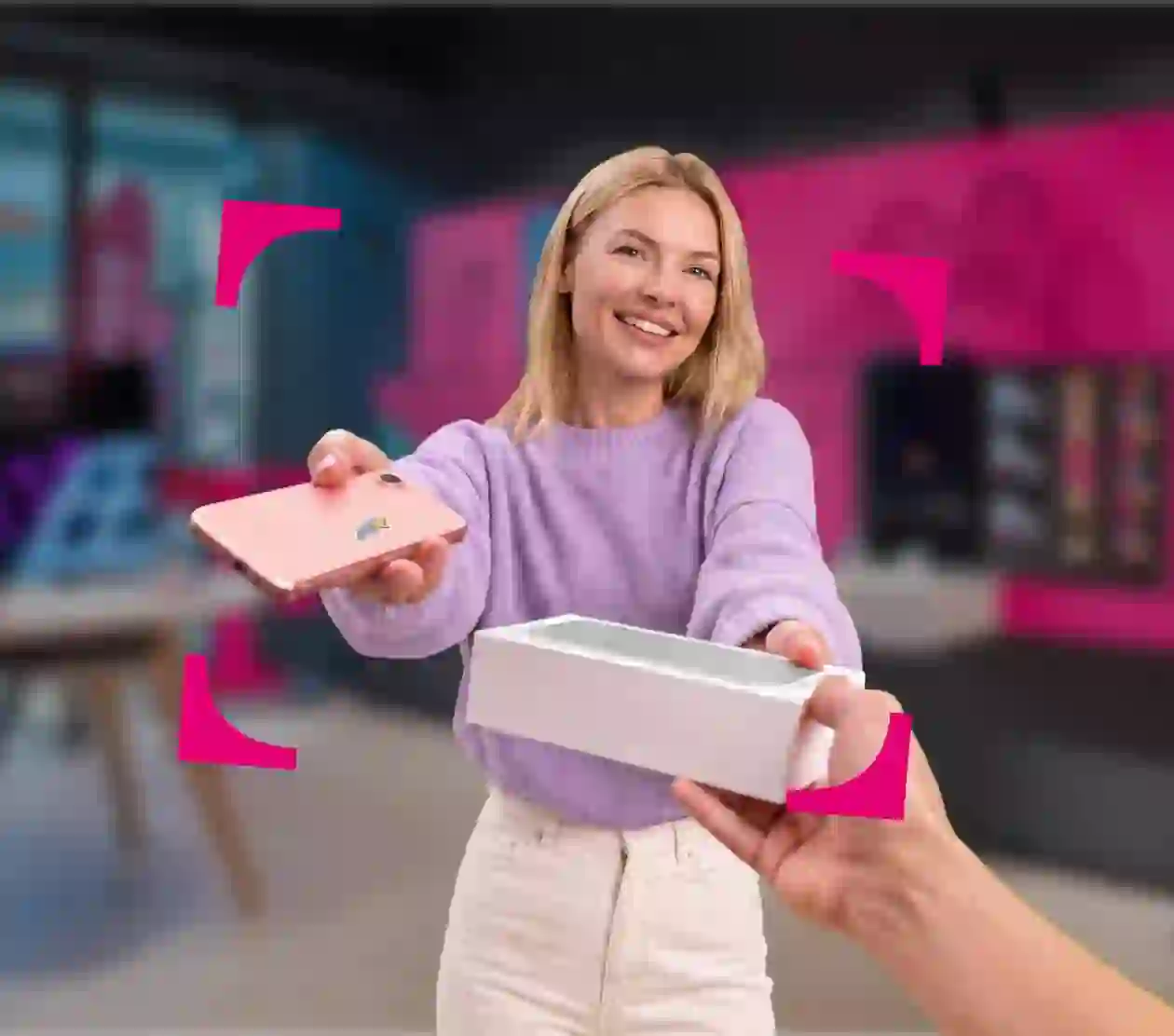 Žena v prodejně T-Mobile předává nový telefon a krabici výměnou za starý telefon